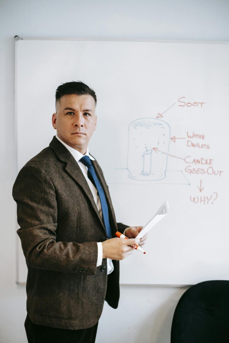 Man in formal attire presenting a scientific diagram on a whiteboard.