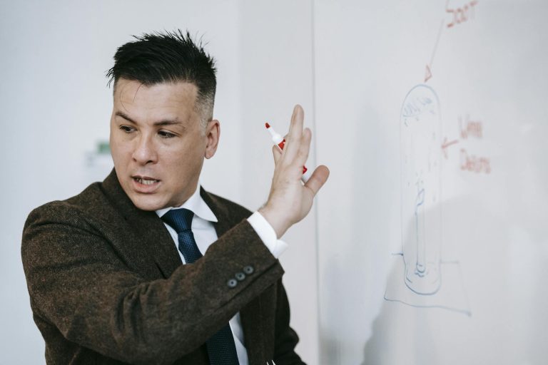 Man in formal attire presenting ideas on a whiteboard in an educational setting.