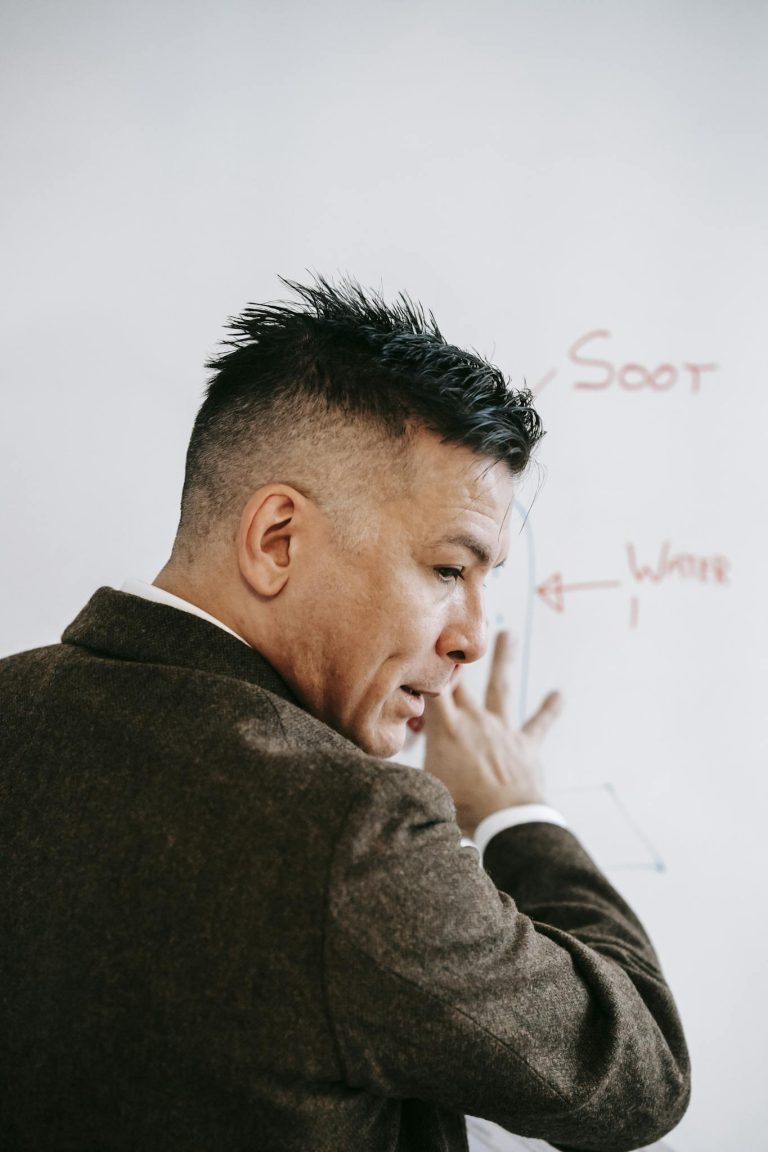 Professional male teacher explaining diagram on whiteboard indoors.